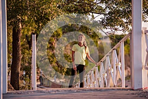 Young woman in sportswear is resting after workout, walking along wooden stairs in the rays of sun