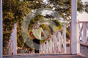 Young woman in sportswear is resting after workout, walking along wooden stairs in the rays of sun