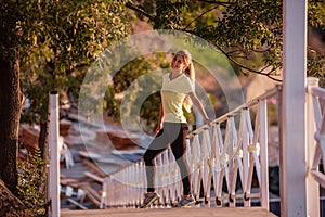 Young woman in sportswear is resting after workout, walking along wooden stairs in the rays of sun