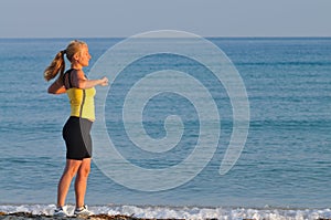 Young woman in sportswear running near still sea edge and smiling