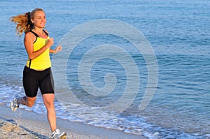 Young woman in sportswear running near still sea edge and smiling