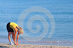 Young woman in sportswear running near still sea edge and smiling