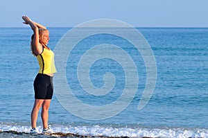 Young woman in sportswear running near still sea edge and smiling