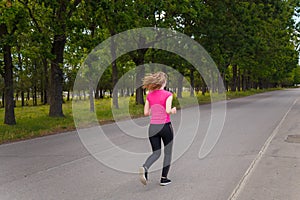 Young woman in sportswear running outdoors on green trees background. Sport, healthy way of life, runners training concept.