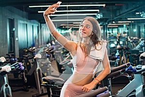 Young woman in sportswear taking selfie photo after cycling training in spin studio.