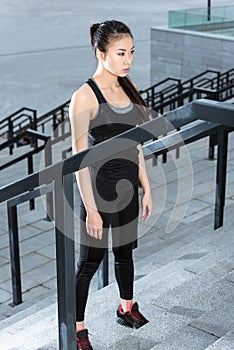 Young woman in sportswear training on stadium stairs and looking away