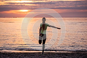 Young woman in sportswear is warming up early in morning on seashore at sunrise. Fitness