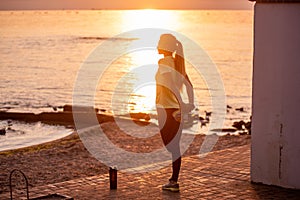 Young woman in sportswear is warming up early in morning on seashore at sunrise. Fitness