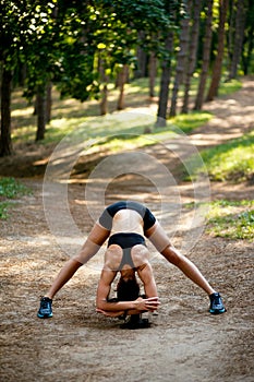 A young woman in sportswear workout outside, doing stretching exercises, of application down in park, forest background