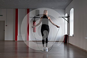 Young woman in sporty black leggings in stylish sneakers does jump rope in a gym. Girl goes in for sports in a fitness studio.