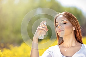 Young woman spraying mist on face with eyes closed