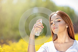 Young woman spraying mist on face with eyes closed photo