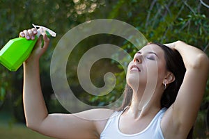 Young woman spraying water on herself from a spray bottle in a summer park