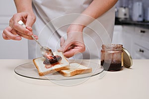 young woman spreading jam on toast, close-up of hands