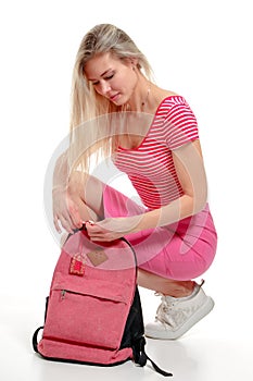 Young woman squatted to get something out of her backpack. Isolation on white background