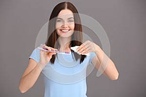 Young woman squeezing toothpaste on brush against grey background