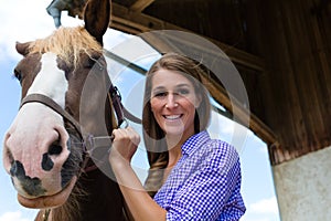 Young woman in the stable with horse at sunshine