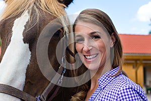 Young woman in the stable with horse in sunshine