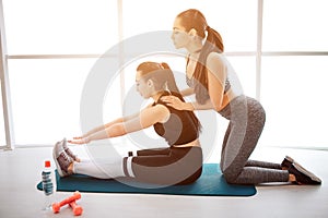 young woman stand on knees behind asian model who keep legs straight. She help her to stretch. Models sit on