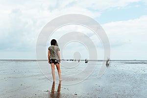 Young woman standing alone in a calm and tranquil beach at low tide