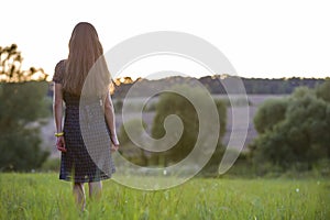 Young woman standing alone on a field with green grass enjoying warm sunset