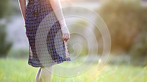 Young woman standing alone on a field with green grass enjoying warm sunset