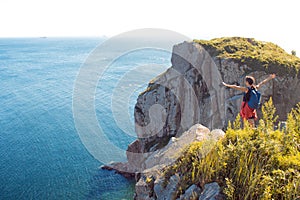 Young woman standing alone on a rocky cliff, arms outstretched. Girl tourist on the background of beautiful wildlife