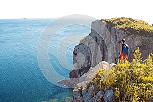 Young woman standing alone on a rocky cliff. Girl tourist on the background of beautiful wildlife, sea and rocks