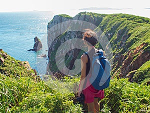 Young woman standing alone on a rocky cliff, Girl tourist photographer on the background of beautiful sea and rocks