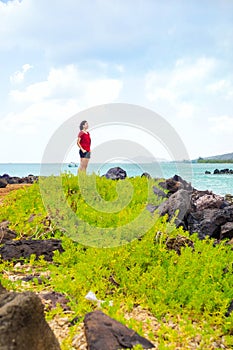 Young woman standing along rocky shore looking out towards ocean