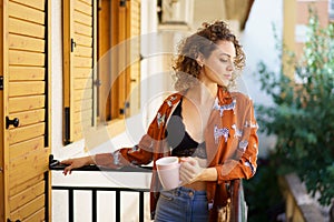 Young woman standing on balcony with cup of coffee