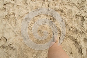 A young woman standing barefoot on the sand on a Sunny summer day. Top view of a beautiful leg. Empty space for text