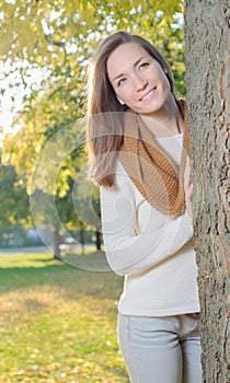 Young woman standing behind tree outdoor in park