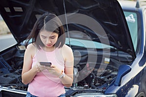 Young woman standing by broken car on the road and using smartphone calling assistance