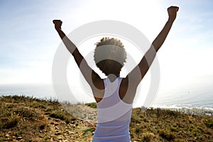 Young woman standing on cliff with her hands raised