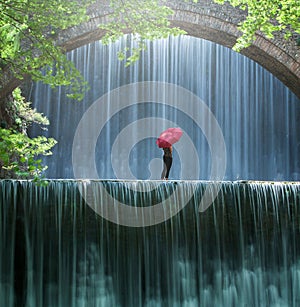 Young woman with a red umbrella standing and looks at the waterfall