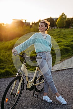 Young woman standing by electro bicycle, concept of commuting and ecologic traveling.