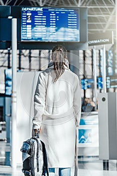 Young woman standing in front of Destination digital board in airport.