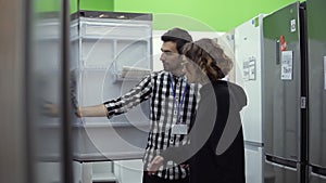 Young woman standing in front the open door of refrigerator with male consultant discussing design and quality before