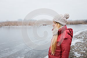 Young woman standing by the frozen lake in winter morning