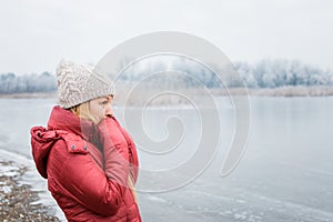 Young woman standing by the frozen lake in winter morning