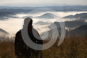 Young woman standing on golden meadow and watching towards the sunrise above mist