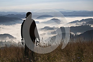 Young woman standing on golden meadow and watching towards the sunrise above mist