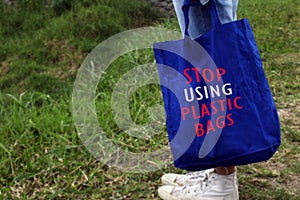 Young woman standing on grass holding a blue women foldable shopping bag with text message - Just say no to plastic bags.