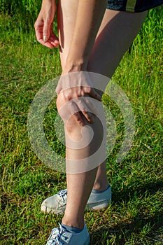 A young woman standing on green grass holds a damaged knee. Sprain or cramps Overstrain an injured person while training or