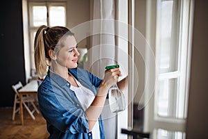 Young woman standing indoors at home, cleaning windows.