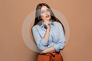 Freestyle. Young girl standing studio isolated on brown touching chin posing to camera pensive