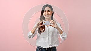 Young woman standing isolated over pink background, holding credit card in her hands