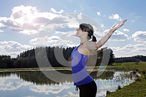 Young woman standing by lake with her arms wide open