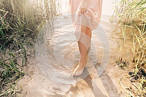 Young woman standing in lake at sunset among fresh reed grass barefooted